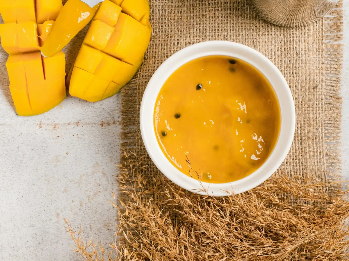 Mango purée in a bowl next to a cut mango